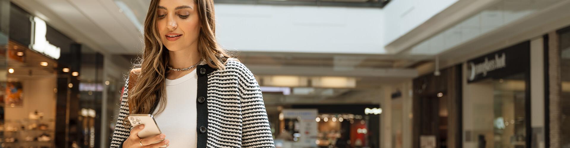 Woman in a striped cardigan looking at her phone in a bright mall concourse