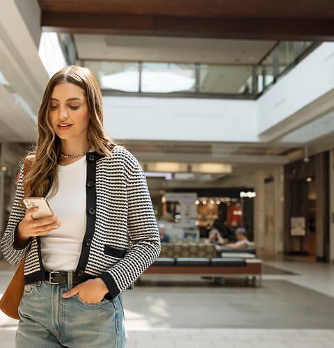 Woman in a striped cardigan looking at her phone in a bright mall concourse