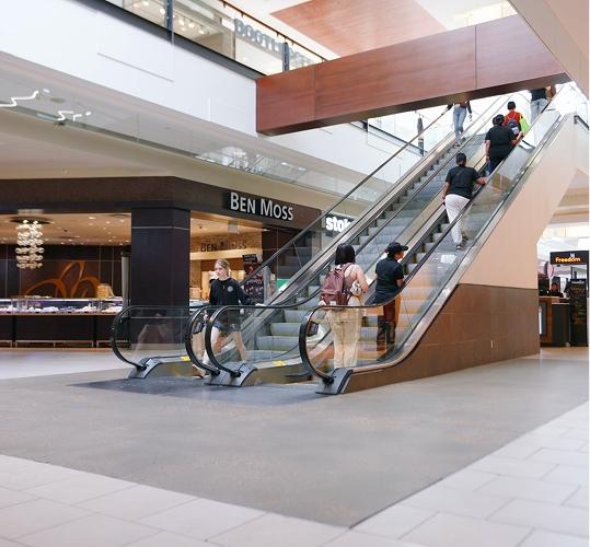 Shoppers riding escalators between mall levels near a Ben Moss store