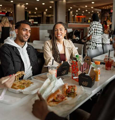 Group of friends laughing together over food at a mall food court table