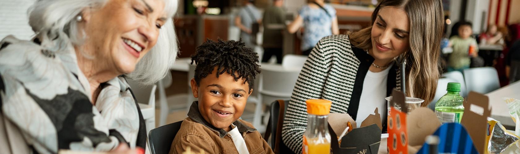 Grandmother, boy and woman sharing a meal at a mall food court table