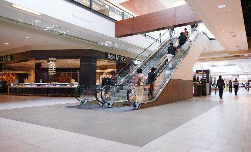 Shoppers riding escalators between mall levels beside a Ben Moss store