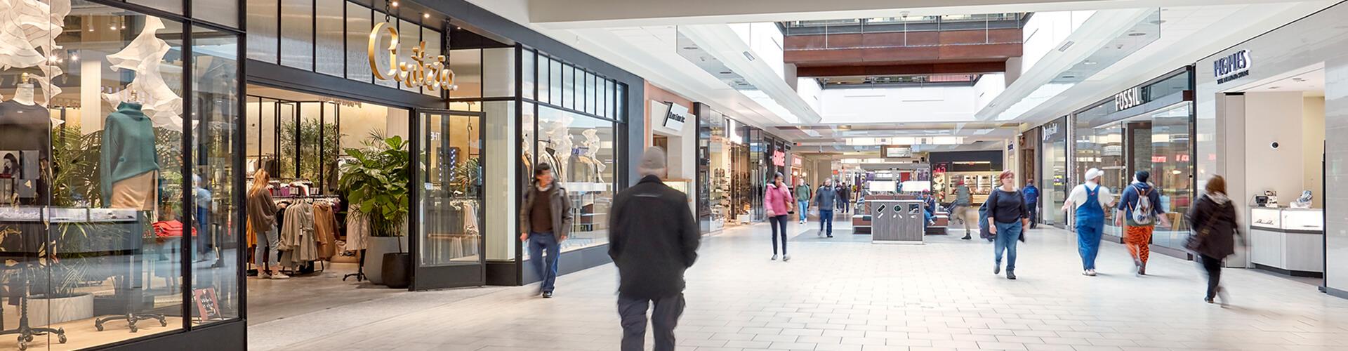 Shoppers walking a mall concourse past Fossil and Peoples storefronts