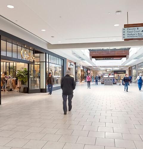 Shoppers walking a mall concourse past Fossil and Peoples storefronts