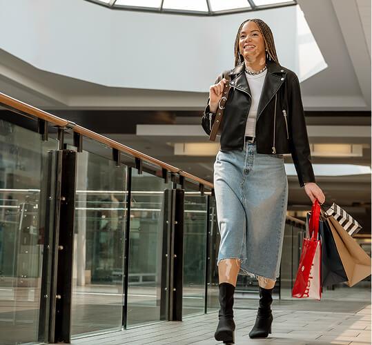 Smiling woman with shopping bags walking along a mall walkway under a skylight