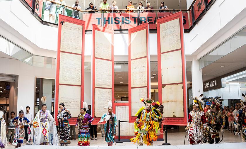 Indigenous dancers performing beside a This Is Treaty treaty document display