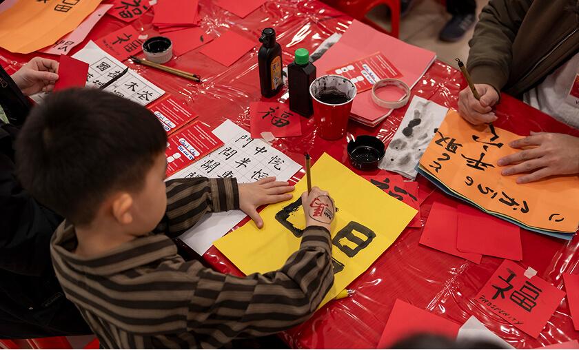 Boy painting Chinese calligraphy at a red Lunar New Year craft table