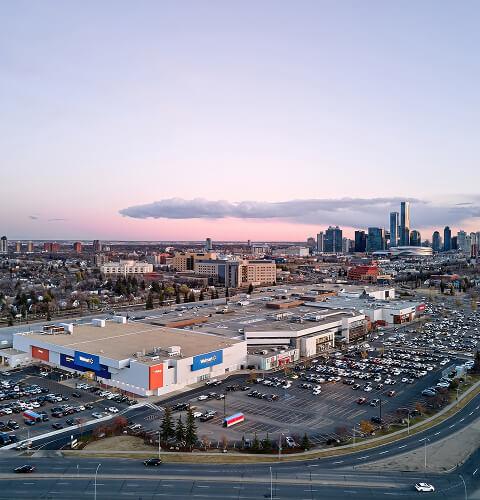 Aerial view of a Walmart-anchored shopping centre with Calgary skyline at dusk