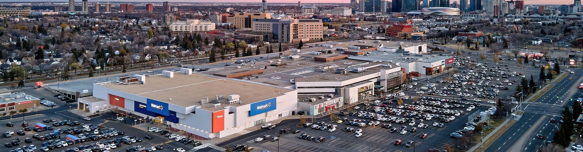 Aerial view of a Walmart-anchored shopping centre with Calgary skyline at dusk