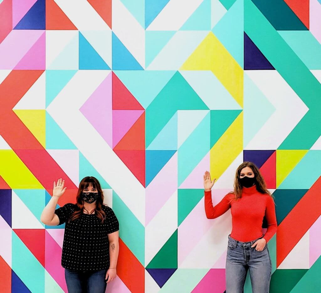 Two women holding up their hand in front of a mural
