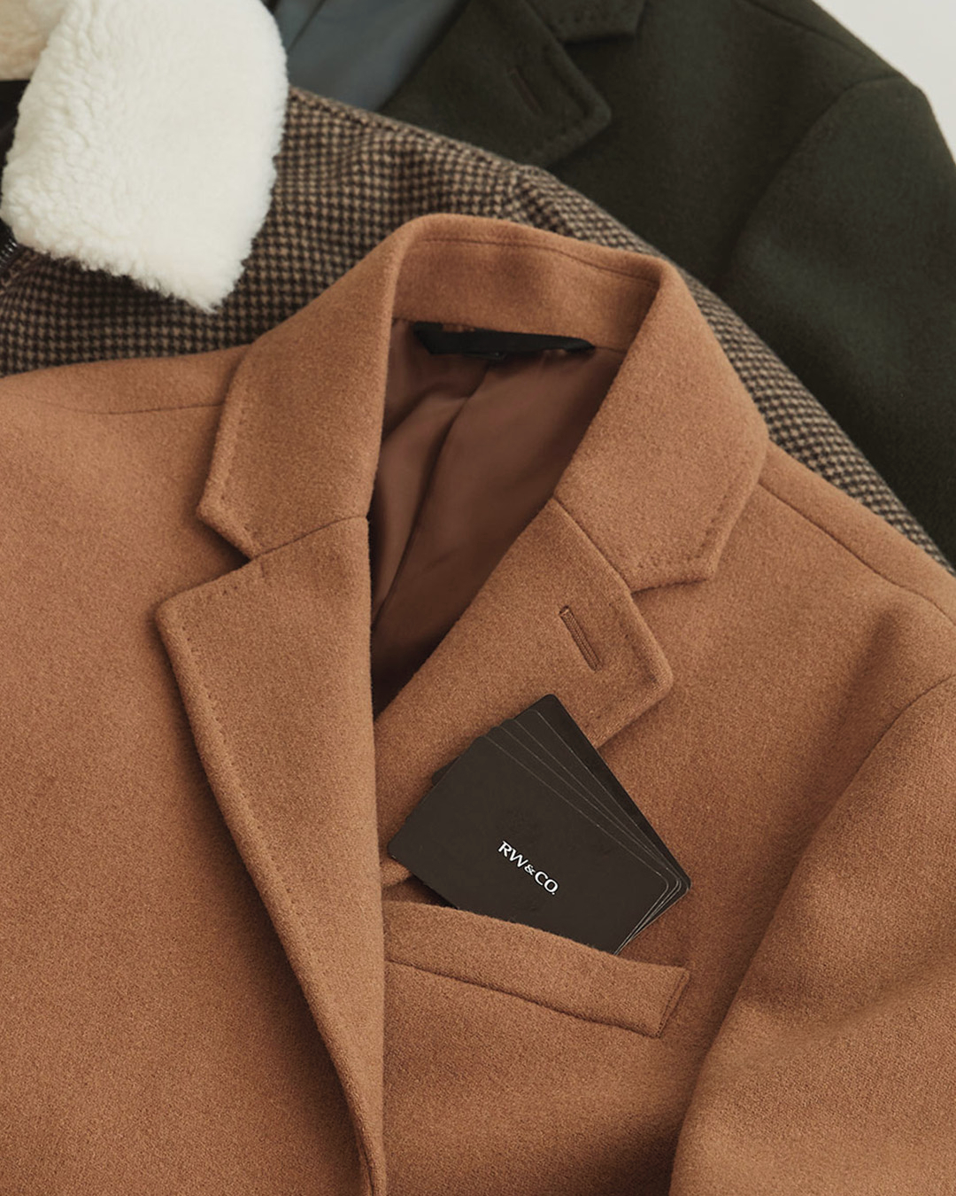 A tan coloured coat from RW&Co lays on top of other clothing.