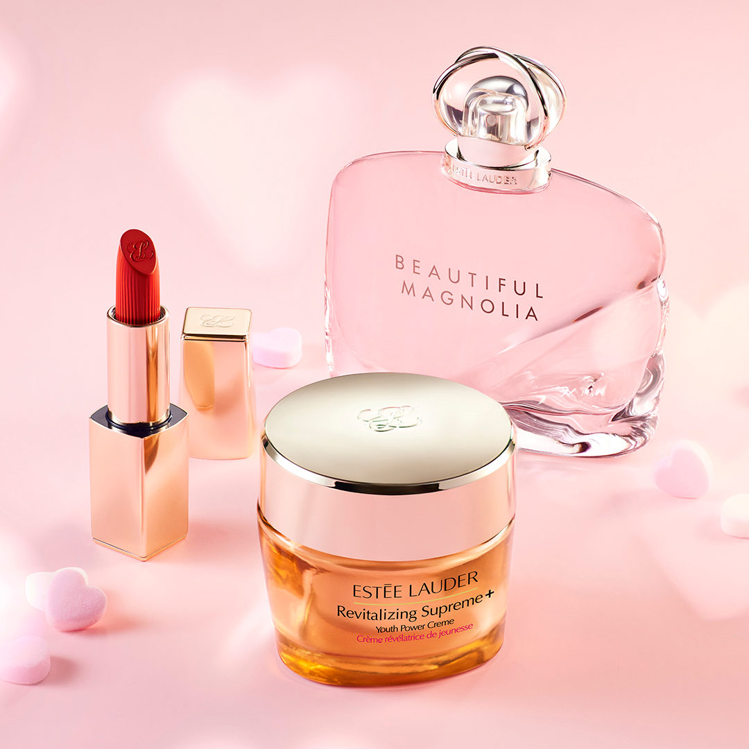 Estee Lauder face cream, lipstick, and perfume are showcased on a light pink background.