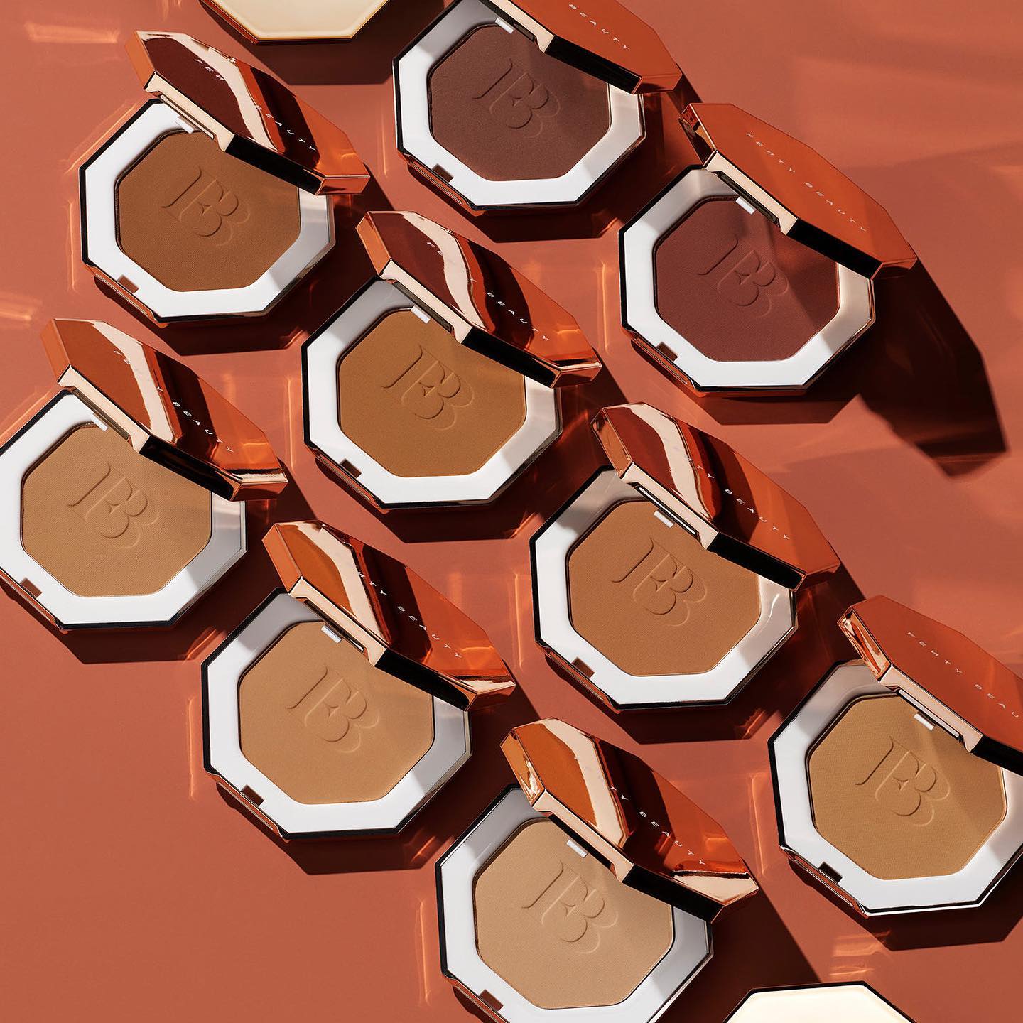 Various skin tone shades of Fenty Beauty Bronzer are displayed on a rust ornage background.