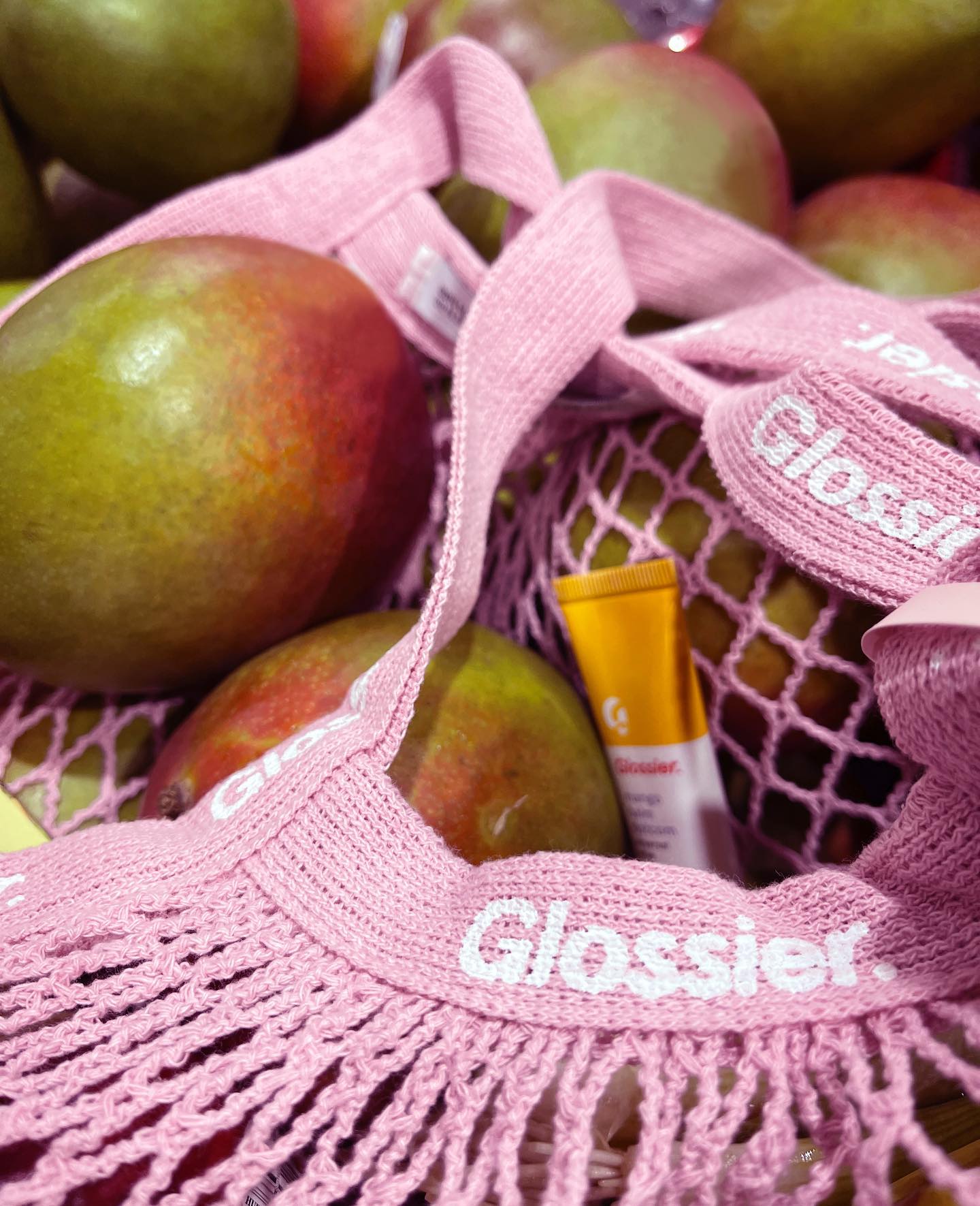 Mangos and Glossier lip products lay in a light pink Glossier fruit bag.