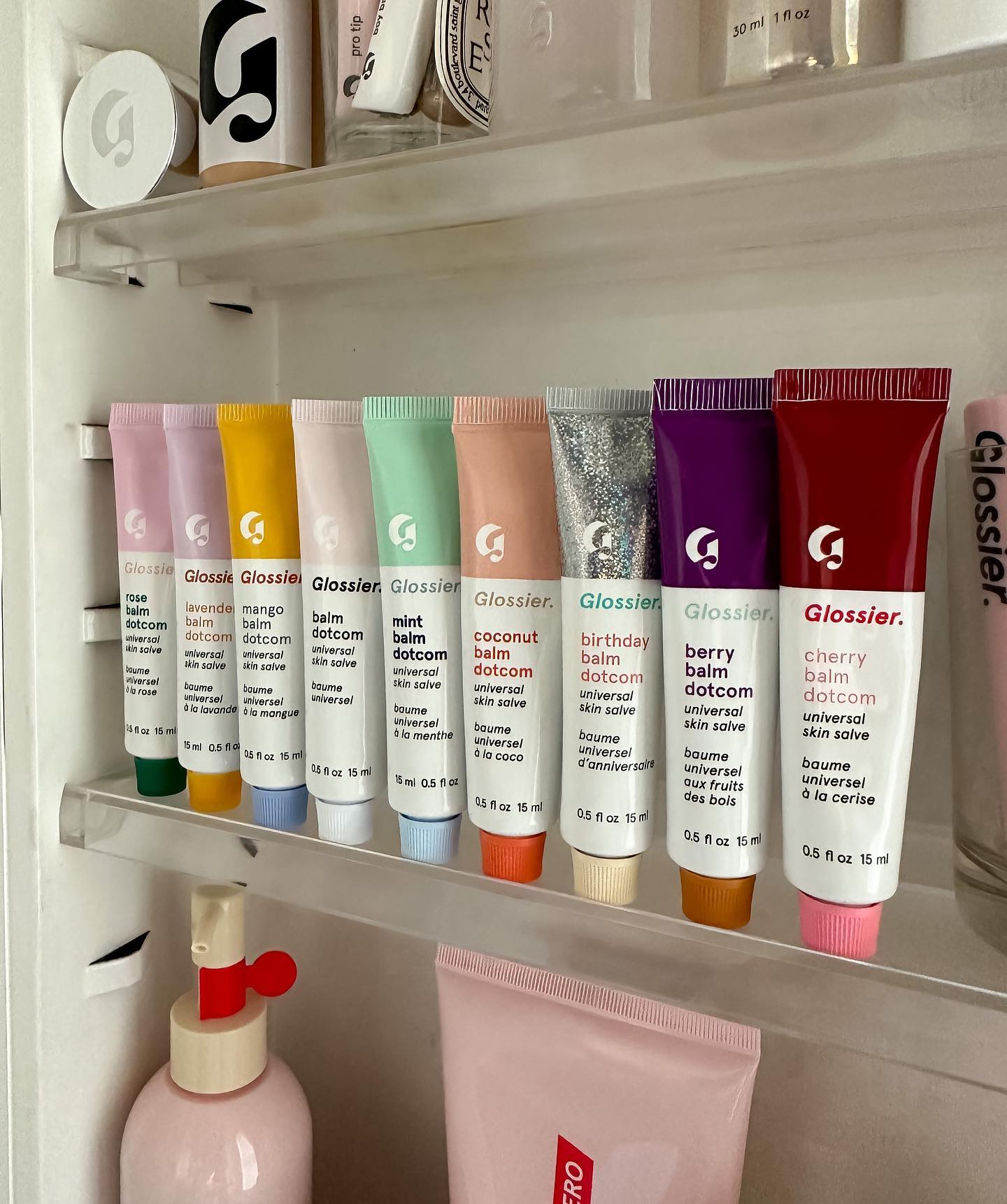 Glossier lip products are set in a line within a bathroom vanity cabinet.
