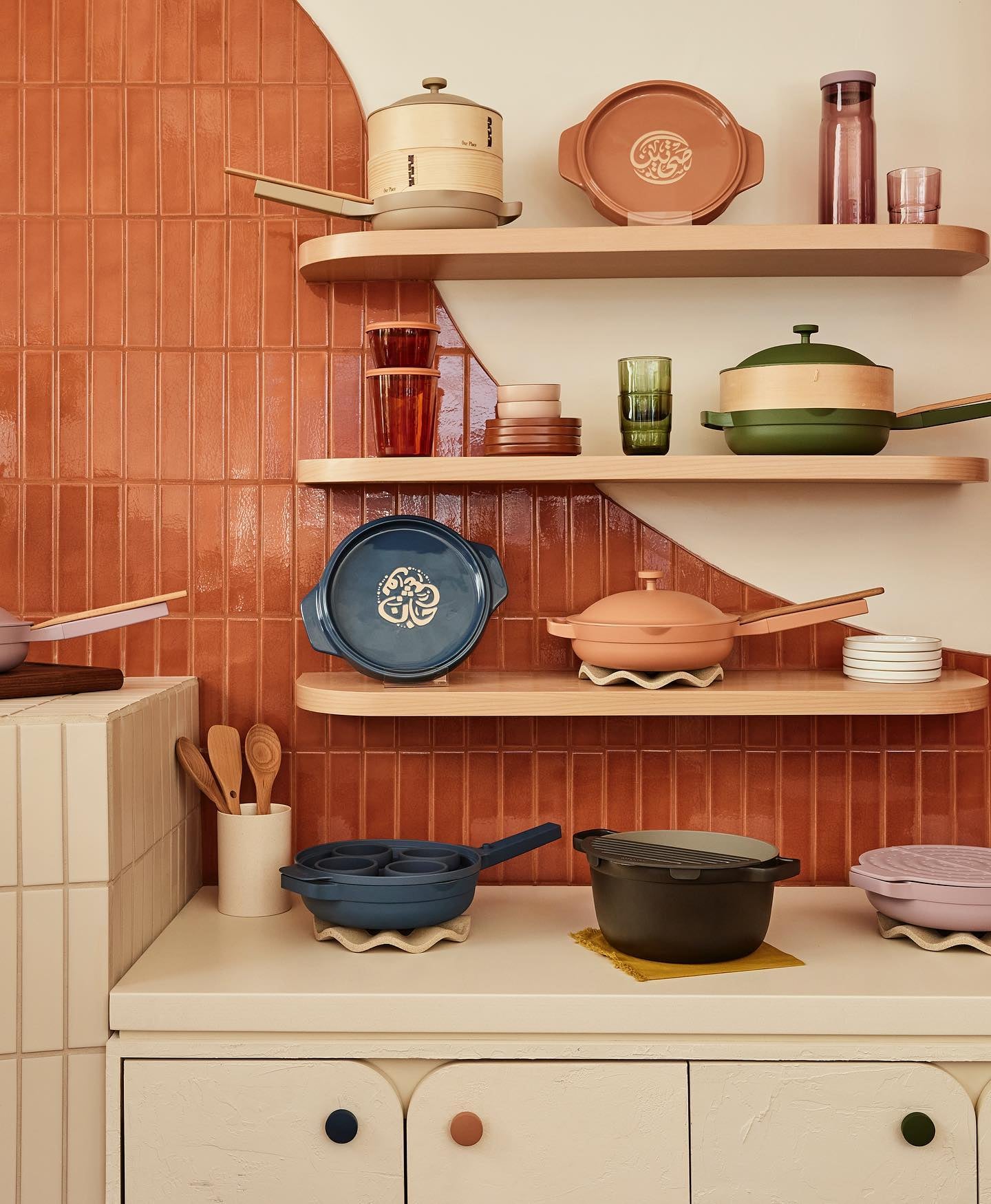 Our Place pots and pans are displayed on a retro-inspired wall with shelves.