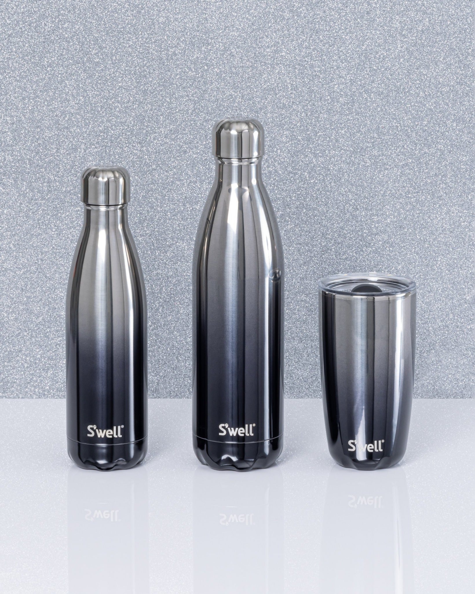 Three different sizes of black to silver ombre S'Well water bottles are on a light background.