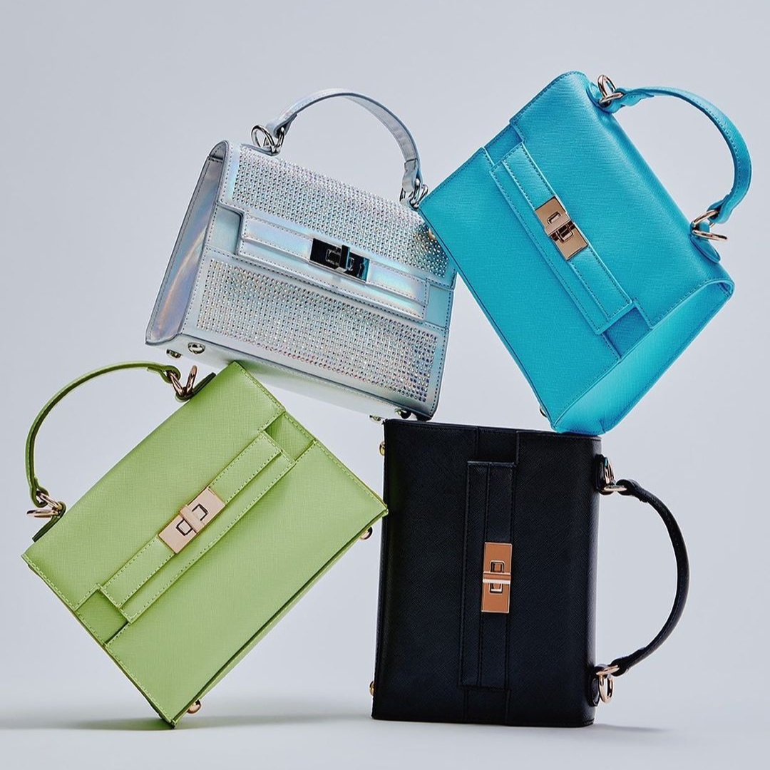 image of four bags stacked atop each other against a white backdrop. They are all top handle bags but in various colours: silver, metallic blue, black and lime green