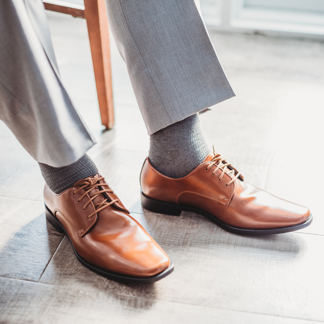 close-up image of a models legs and feet. he wears grey dress pants, grey socks and brown leather dress shoes