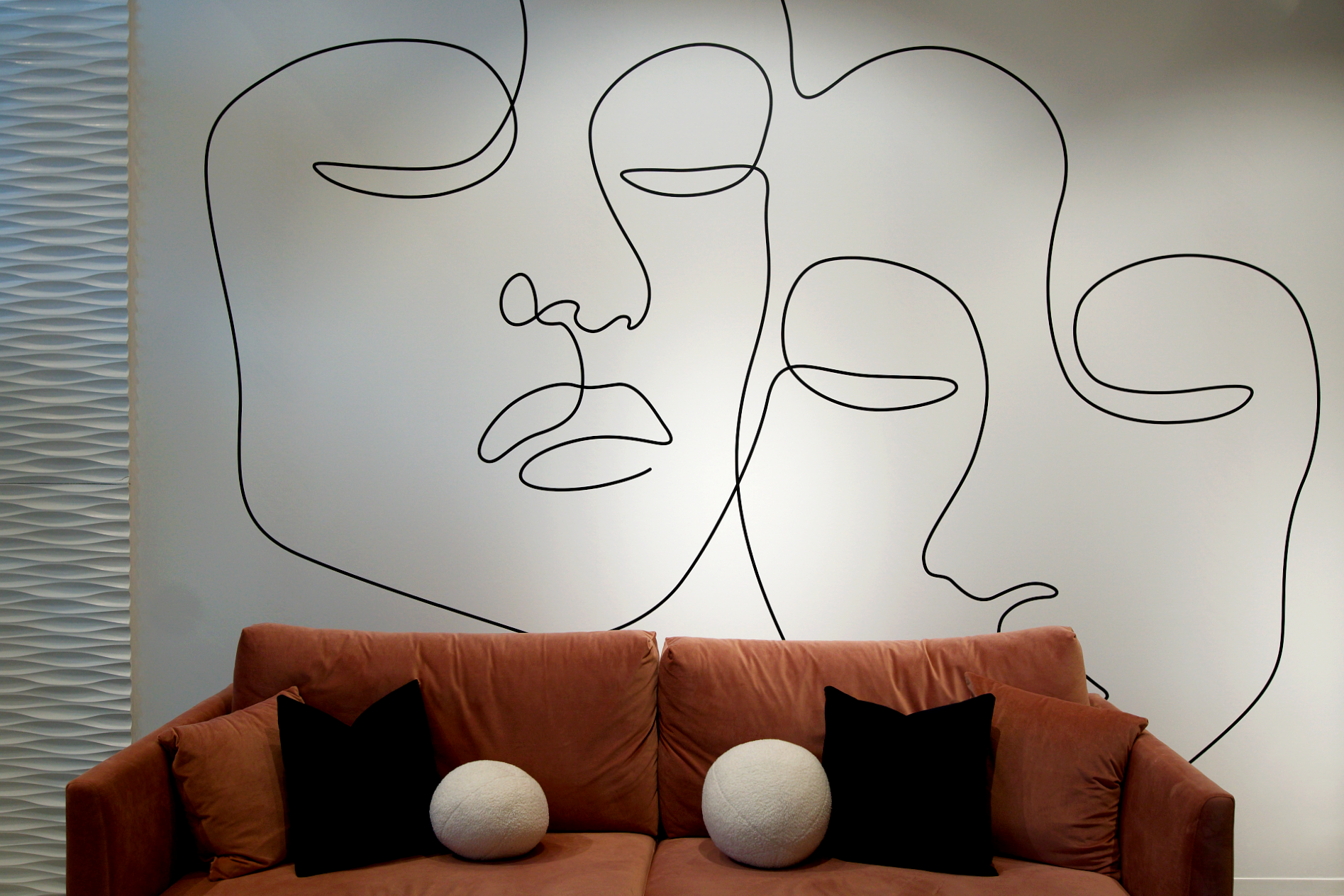 brown couch with decor pillows in front of one line drawing of two faces on wall at a spa
