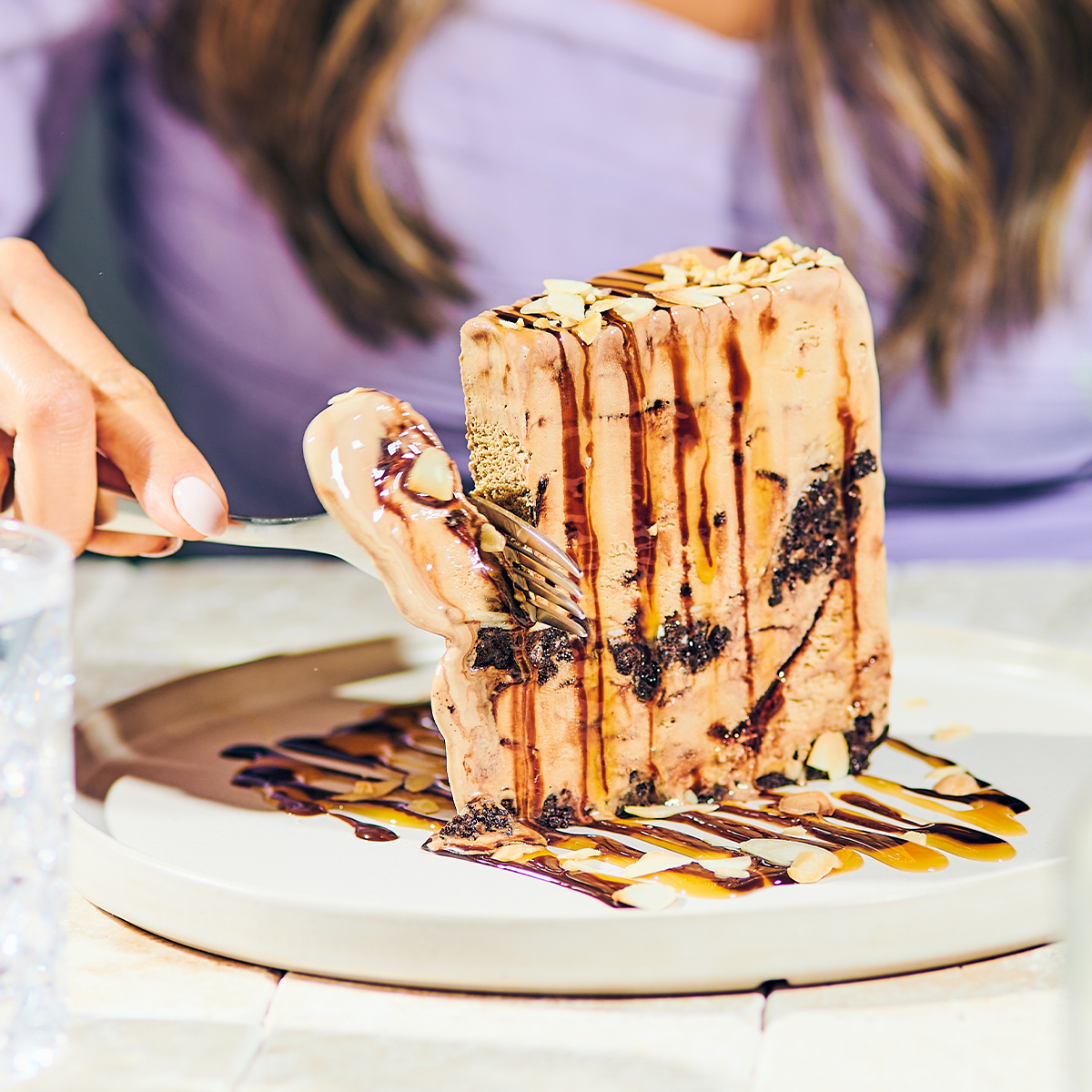 person cutting ice cream cake with chocolate and caramel sauces