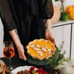 person holding a pumpkin pie on a table of plated food and decor