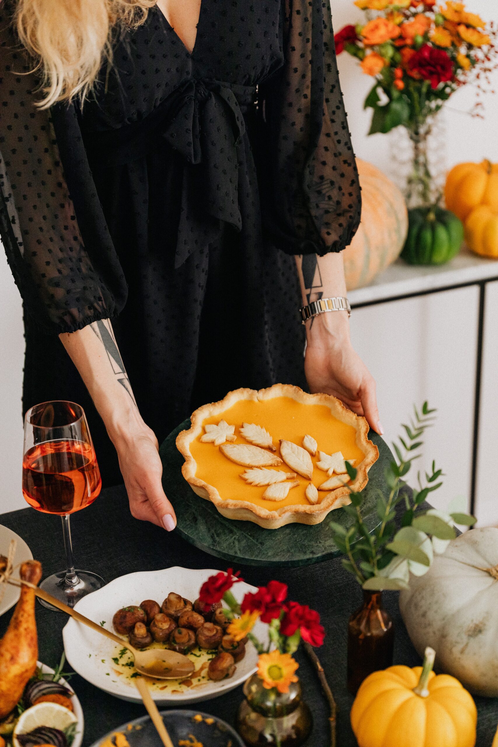 person holding a pumpkin pie on a table of plated food and decor
