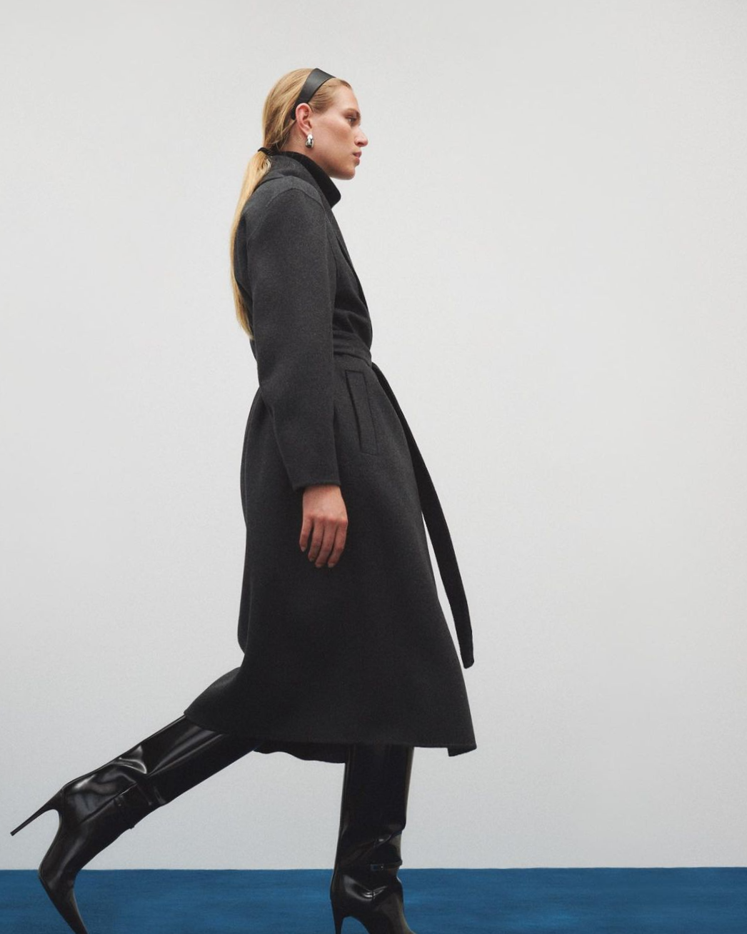 model wearing long black coat with tall black leather boots