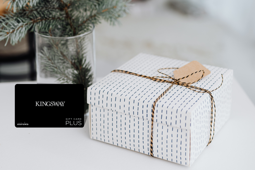 promotional image featuring a black kingsway gift card. beside the gift card is a present wrapped in white wrapping paper and behind the gift card is a vase with pine tree branches.
