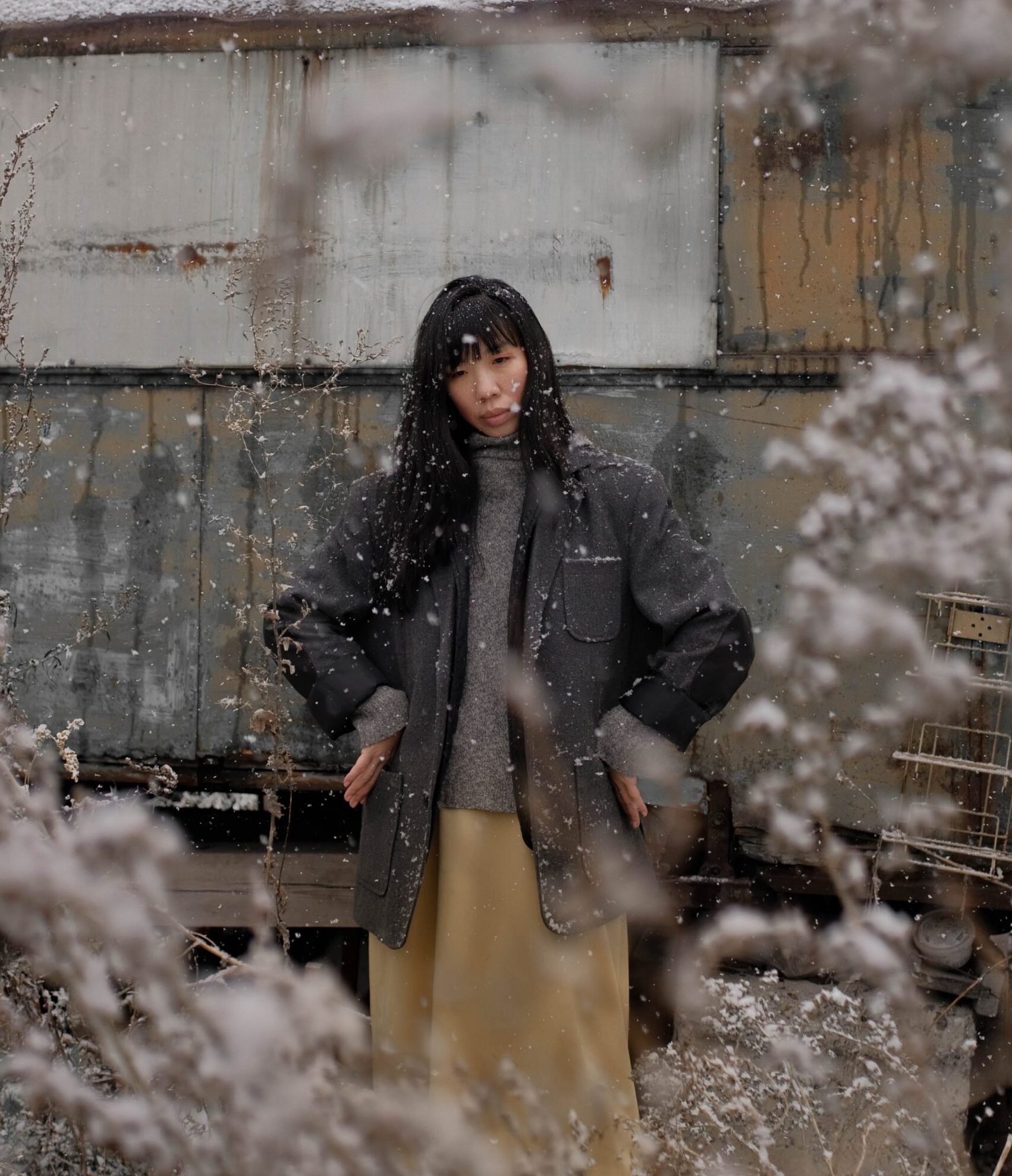 model standing outside in snow, wearing a long coat and skirt