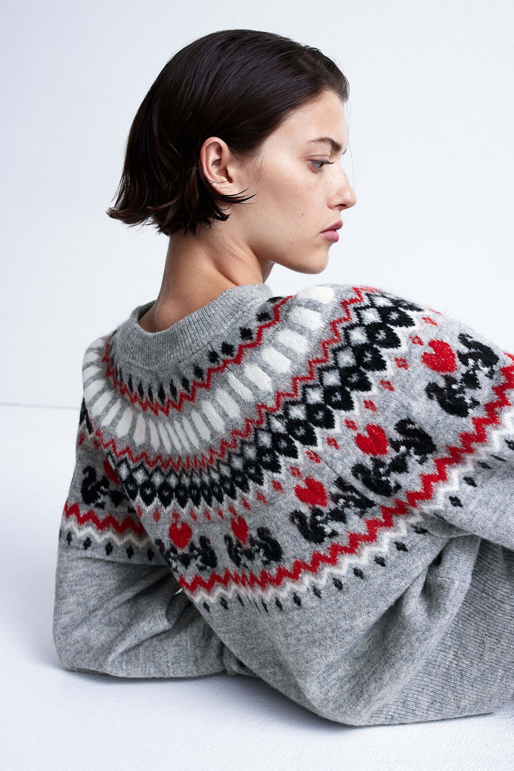 model wearing grey jacquard-knit sweater with red, white and black patterns