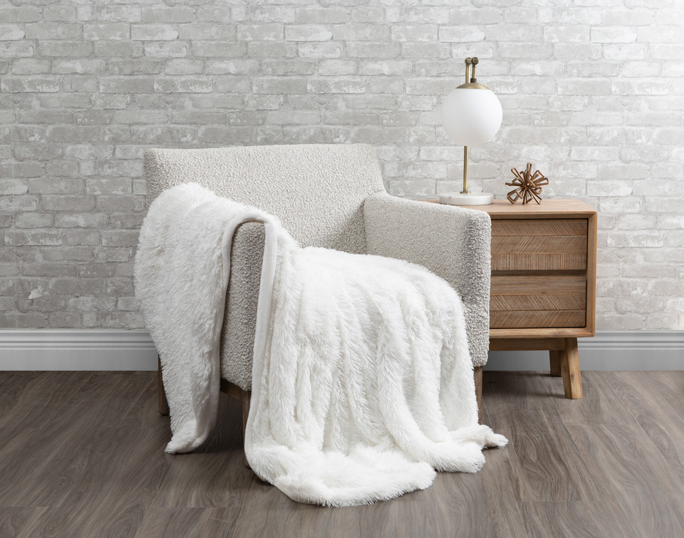 grey living room armchair with white furry throw, beside a table lamp and decor on a side table