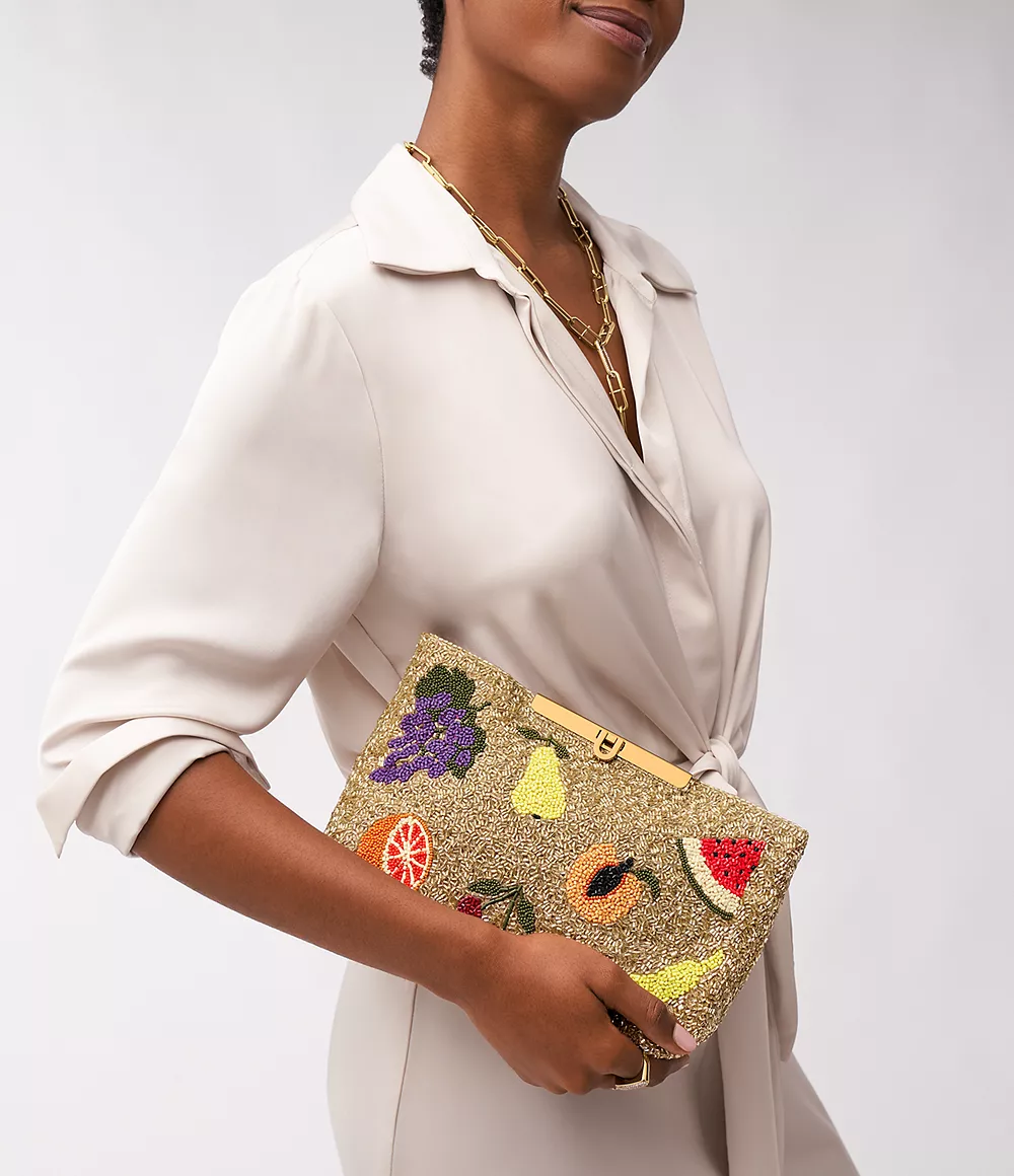 model wearing cream coloured dress and holding fruit-patterned clutch
