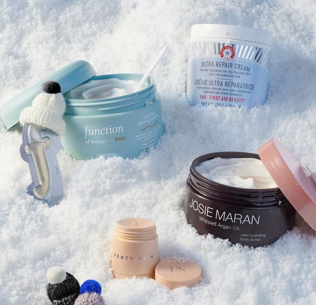 containers of skincare by First Aid Beauty, Function of Beauty, Josie Maran and Fenty Skin displayed in snow