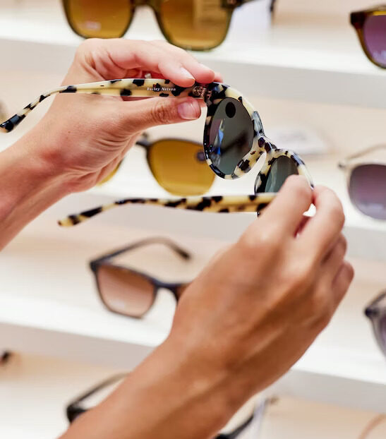 model holding a pair of cheetah print sunglasses in front of sunglasses display