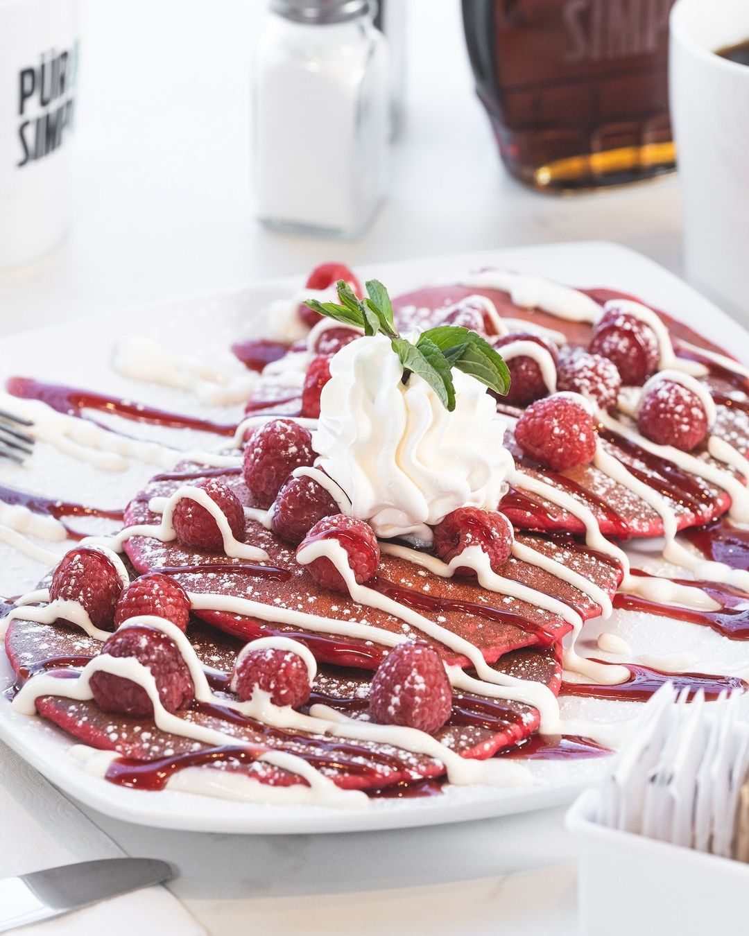 red velvet pancakes topped with raspberries, sauces and whipped cream