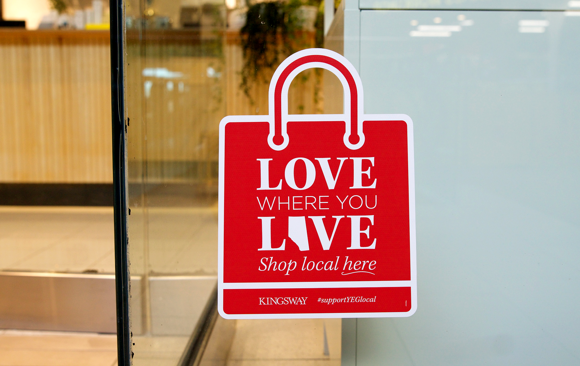 Red shopping bag window decal promoting 'Love Where You Live' message for supporting local businesses