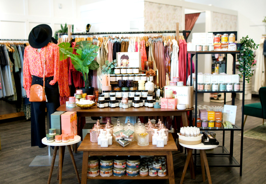 table display in storefront with candles and home goods with women's clothing racks behind