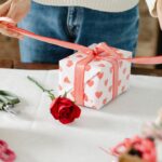 woman wrapping present with white wrapping paper and pink patterned hearts and a rose