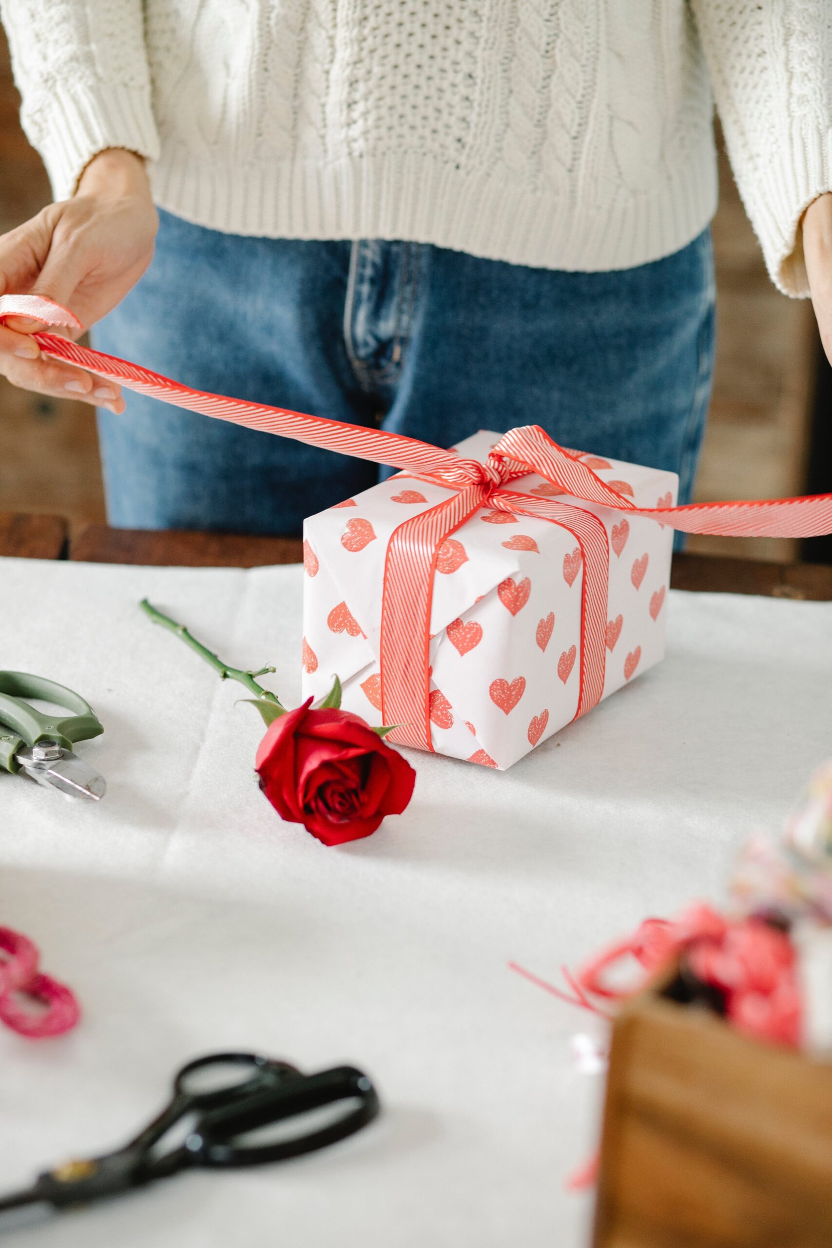 woman wrapping present with white wrapping paper and pink patterned hearts and a rose
