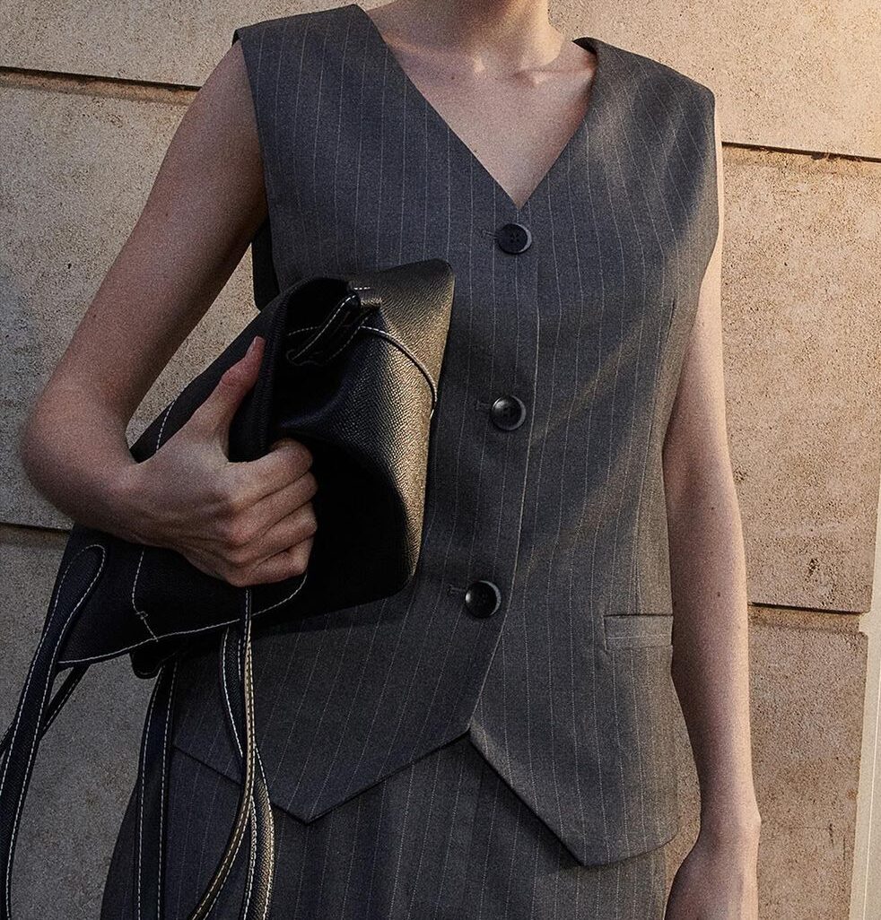 model wearing buttoned gray vest and pants while holding a black purse