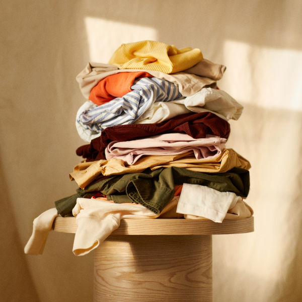 variety of clothing stacked on wooden table, including sweaters and pants