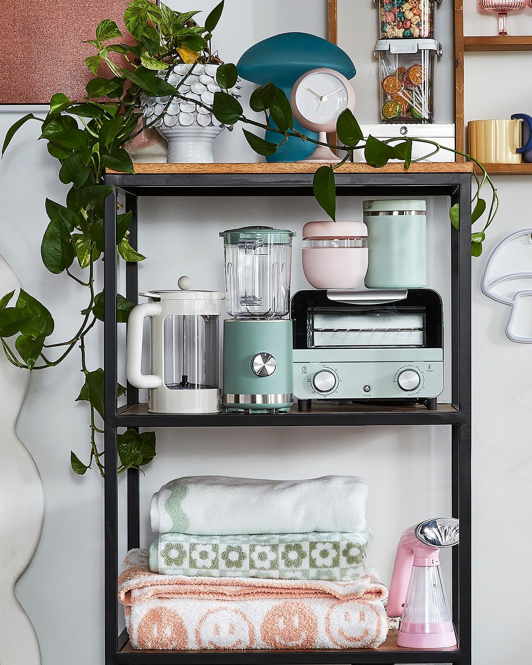 black shelf holding a variety of small pastel-coloured kitchen appliances and bath towels