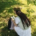 school girl wearing green sweater vest and white skirt with backpack reading a book