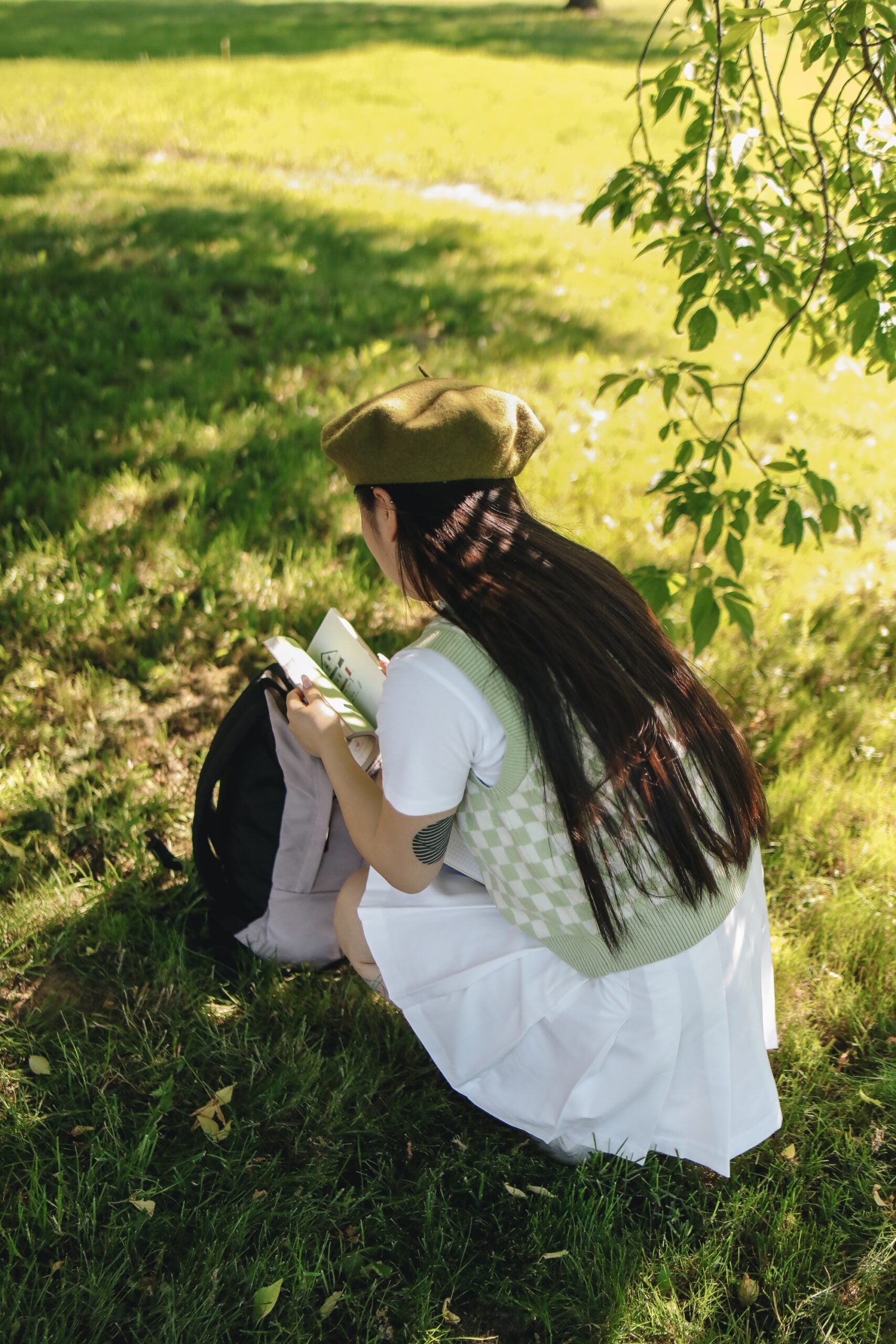 school girl wearing green sweater vest and white skirt with backpack reading a book