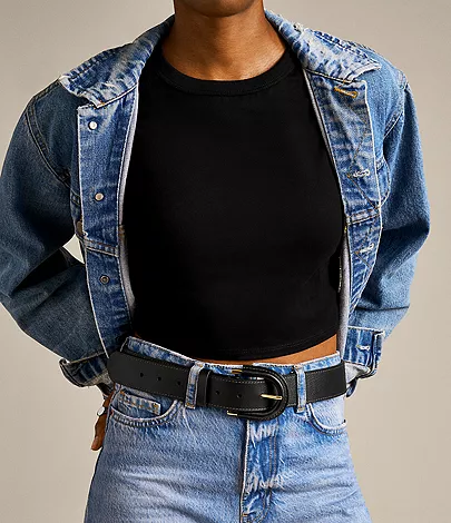 model wearing black top, blue jean jacket, jeans, and black belt with large buckle