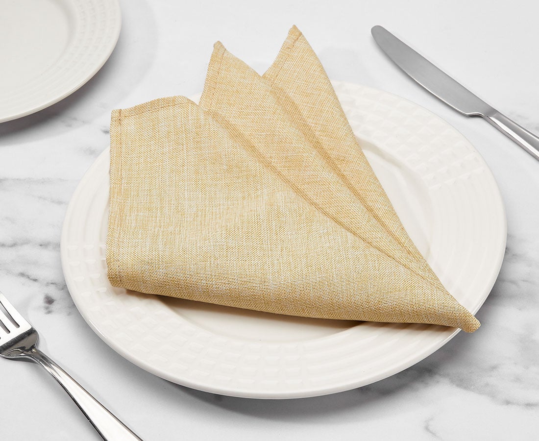 folded gold cloth napkin on white dining plate