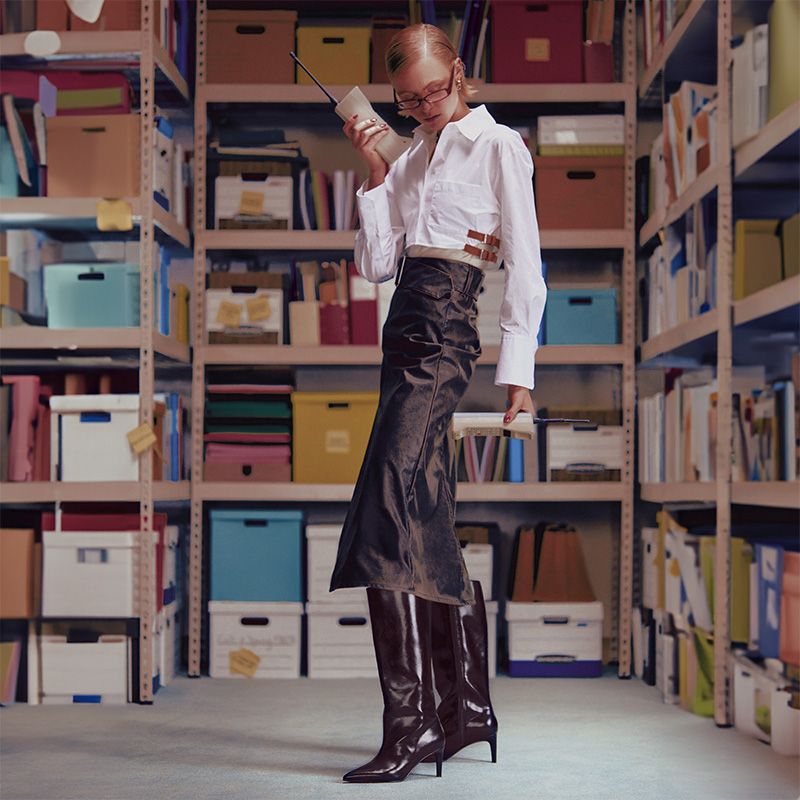 model wearing white button up shirt, long brown pencil skirt, and tall brown leather heel boots