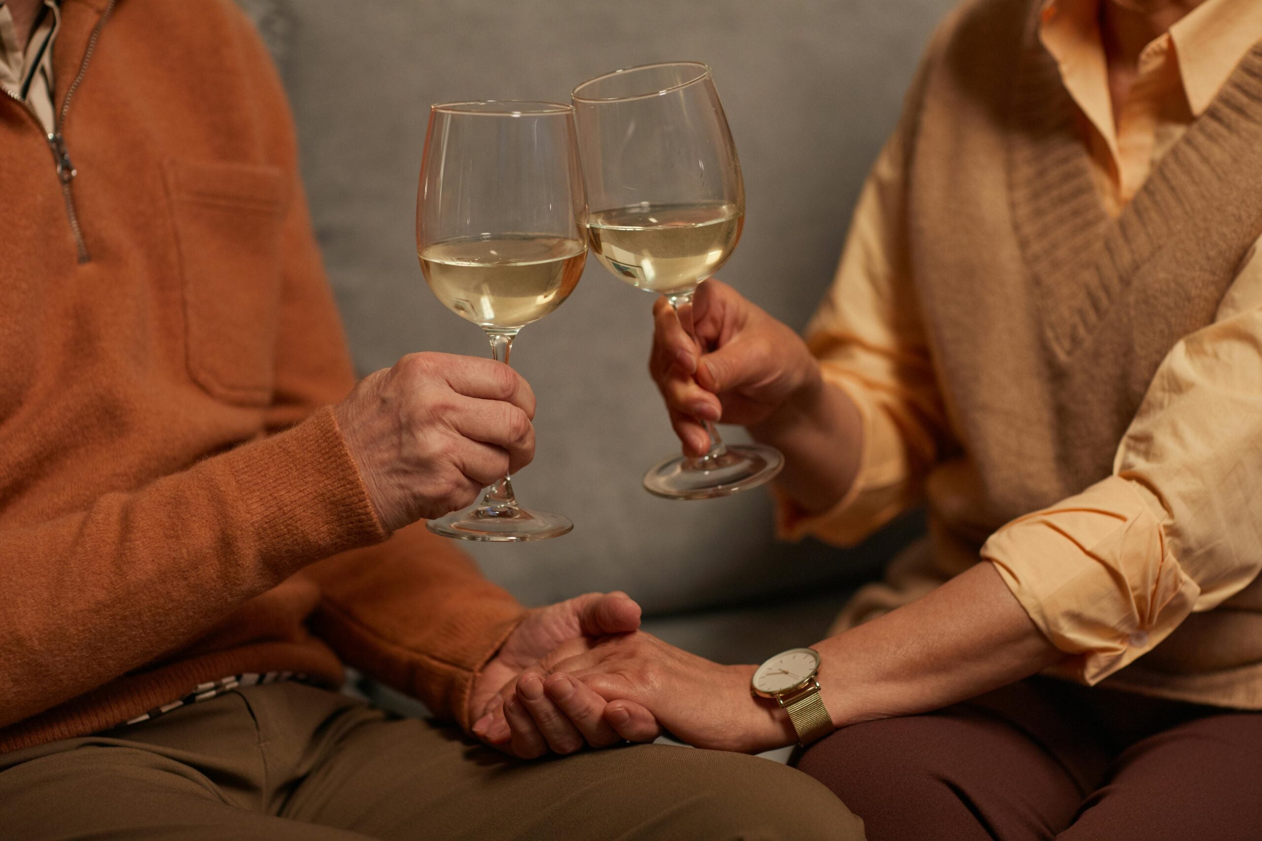 A couple holding hands and clinking white wine glasses