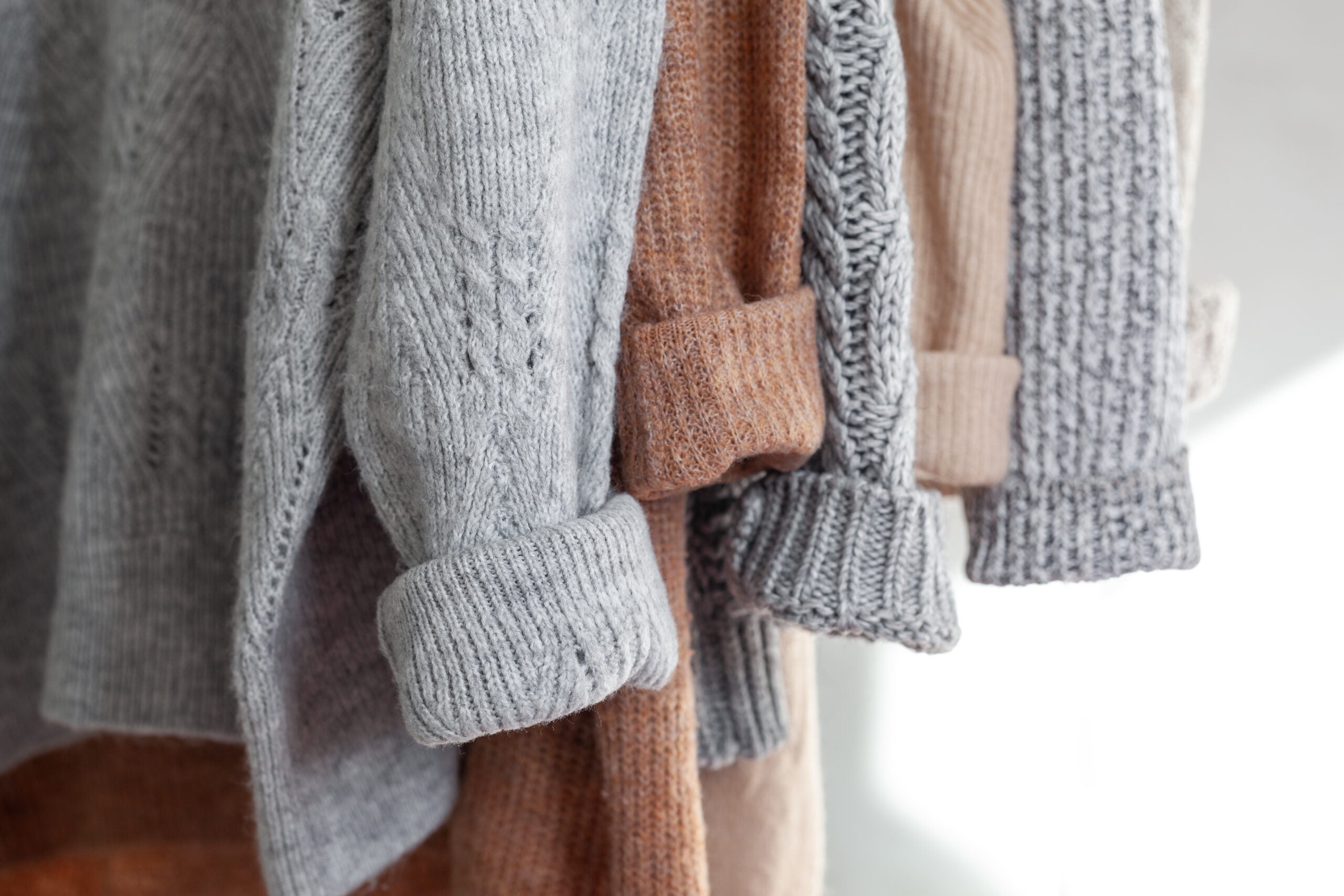 Brown and grey knit sweaters hanging in a closet, with cuffed sleeves